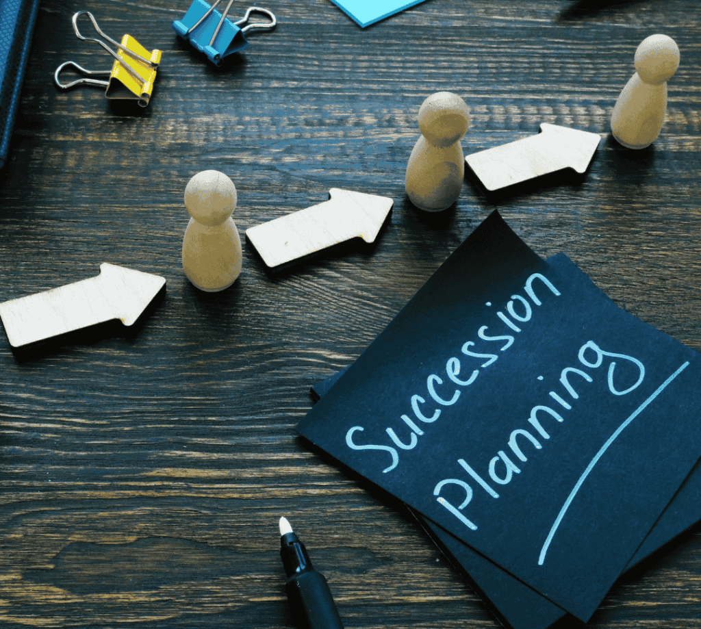 A desk with arrows, marker, clips, and pos it that says "Succession Planning"